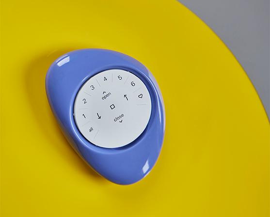 Blauwe Luxaflex® Pebble® PowerView® afstandsbediening op gele tafel dopamine decor interieur