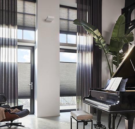 Luxaflex vitrage gordijnen met Duette Shades plisségordijnen zwarte kozijnen hoog plafond witte muren gietvloer modern interieur piano vleugel