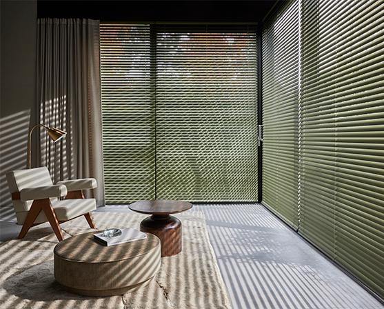 Luxaflex groene aluminium jaloezieën mid century modern interieur betonvloer tapijt walnoot houten stoel en salontafel