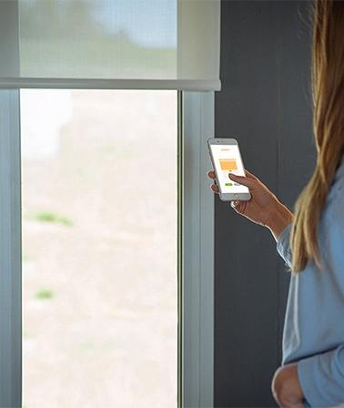 vrouw gebruikt Somfy Tahoma app slimme rolgordijnen